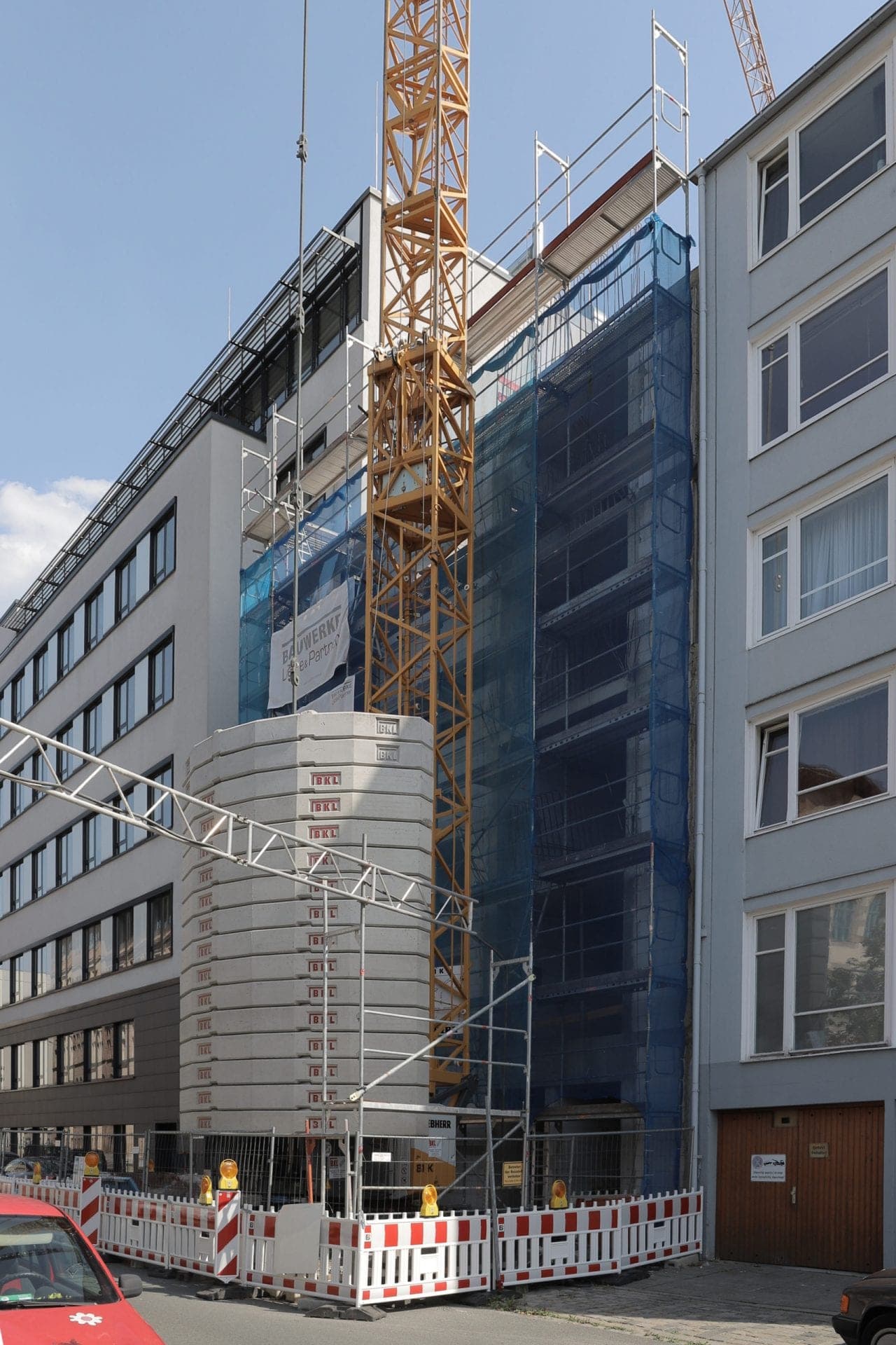 Construction site in the infill plot with a tower crane, crane ballast and the scaffolded shell between neighbours