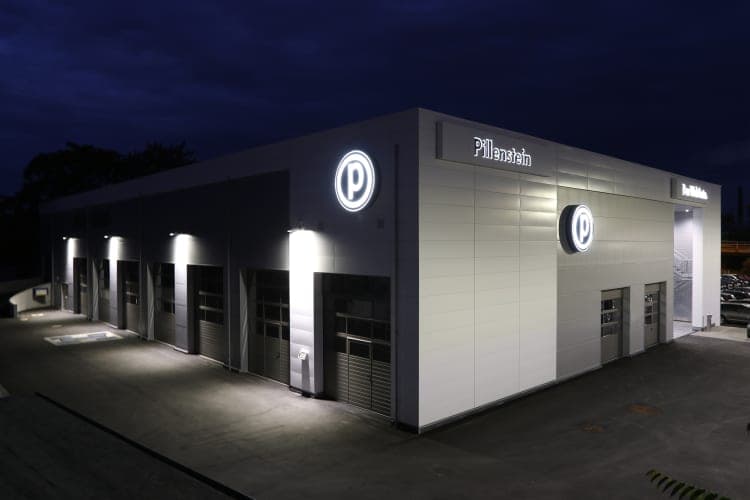 Workshop wing at night with illuminated round logos, Pillenstein lettering and sectional doors
