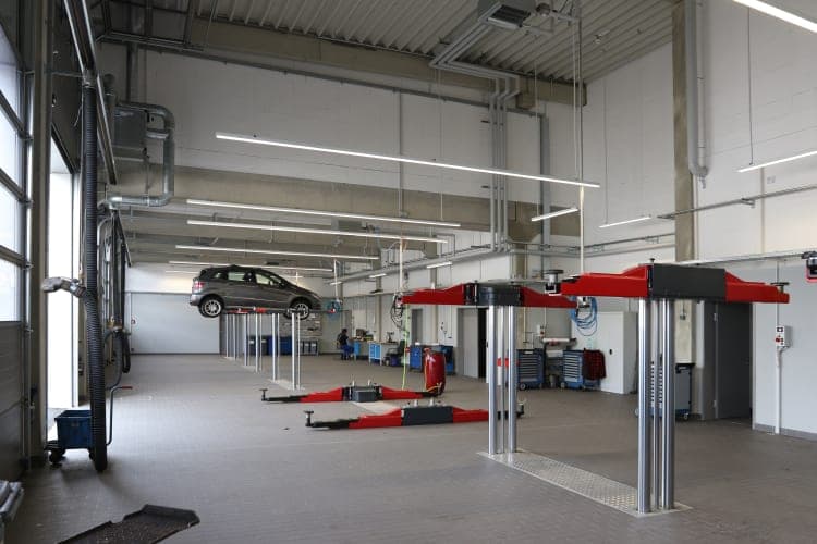 Workshop hall with a vehicle on a lift and further red vehicle lifts beneath strip lights