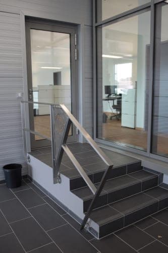 Short flight of steps with a stainless steel handrail and dark tiles in front of the glass office door