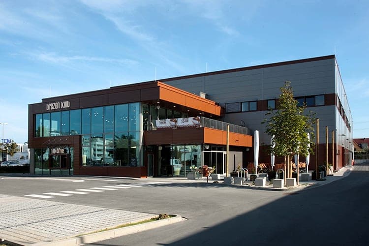 Street view of the head building with glazed façade, lettering and first-floor terrace in sunshine