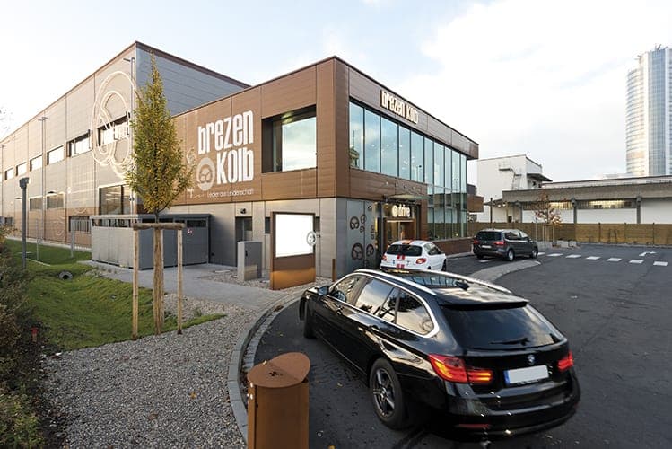 Building corner with façade logo and drive-through lane, a high-rise tower in the background