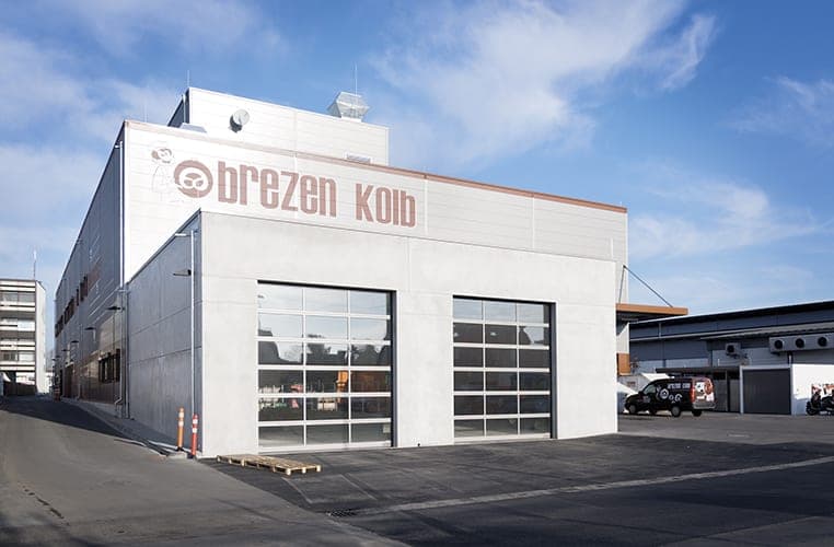 Rear of the production hall with a pale façade, lettering and two glazed sectional doors