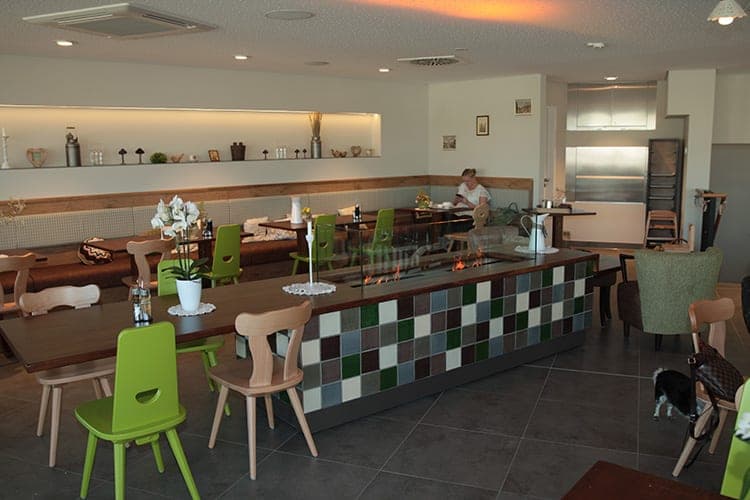 Dining area with an upholstered bench, green wooden chairs and a long table with a tiled fire pit