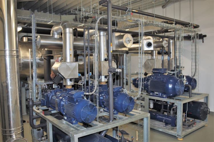 Plant room with blue units on steel frames and an extensive network of pipework