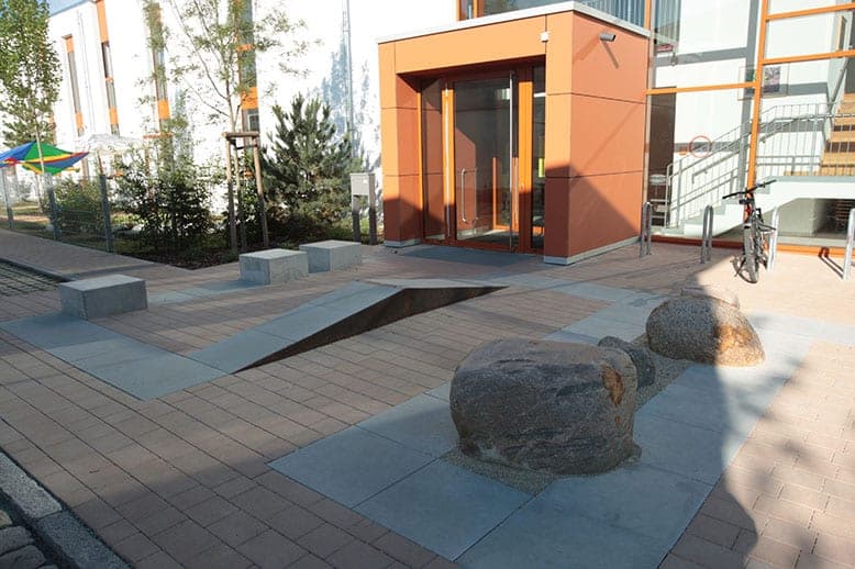 Paved forecourt with boulders and stone seating blocks in front of the orange-clad entrance porch