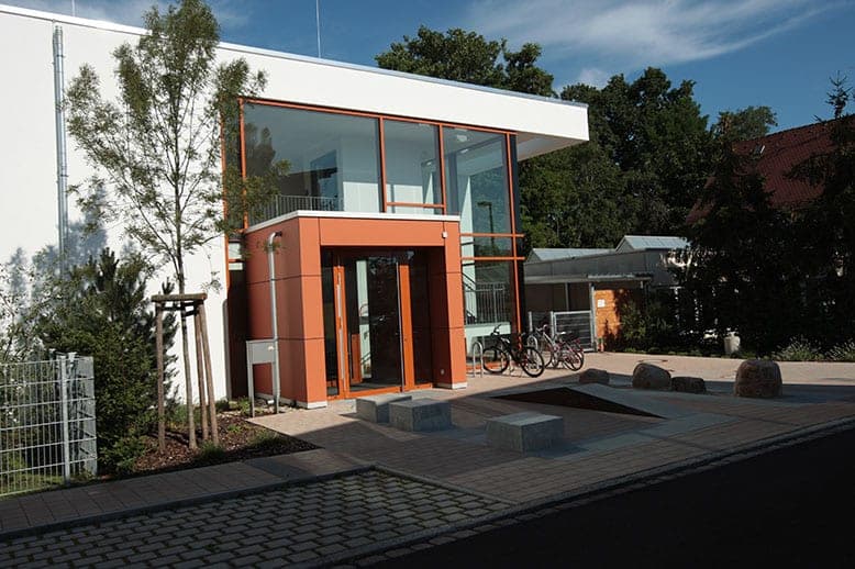 Side view of the entrance with the orange porch, glazed façade to the stairwell and cycle stands