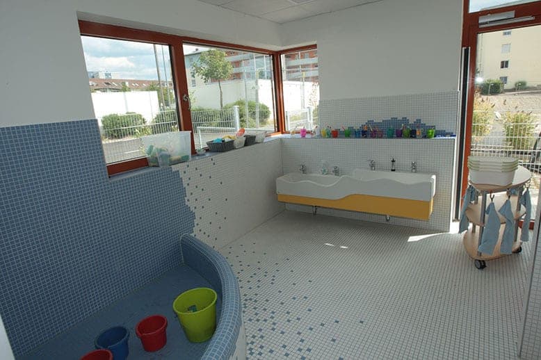 Nursery washroom with a curved child-height washbasin, splash corner and timber-framed corner windows