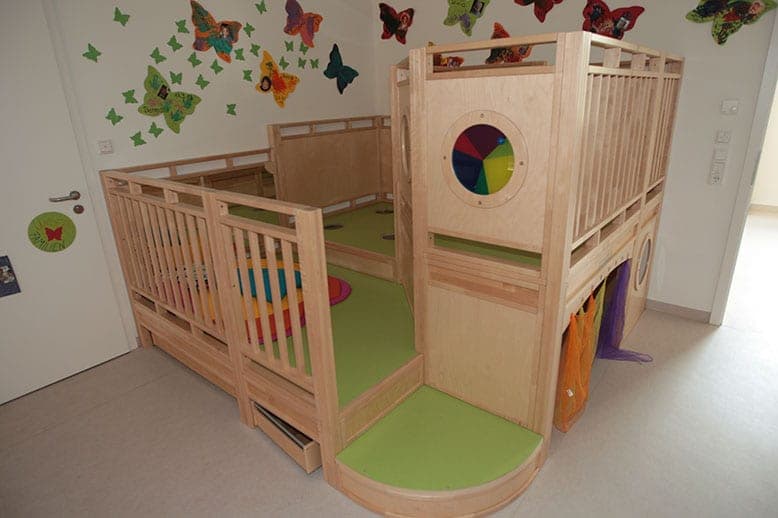 Crèche room with a two-level wooden play platform and butterfly decorations on the wall