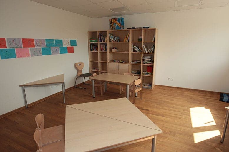 Group room with parquet floor, a bookcase, trapezoidal tables and children's drawings on the wall