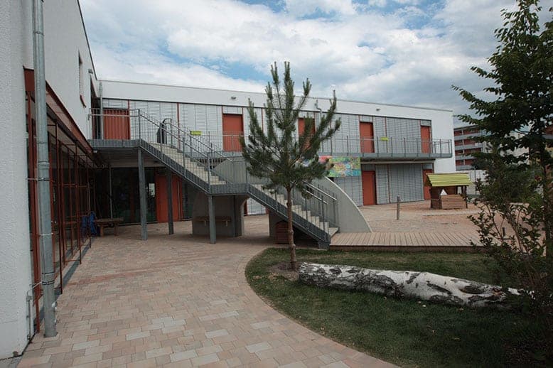 Upper-floor access gallery with a steel staircase, timber deck and birch log on the courtyard lawn