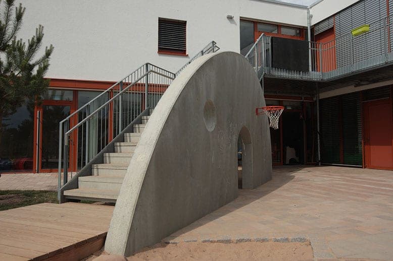 Concrete arch with a passage and basketball hoop in front of the external stair and glazed ground floor
