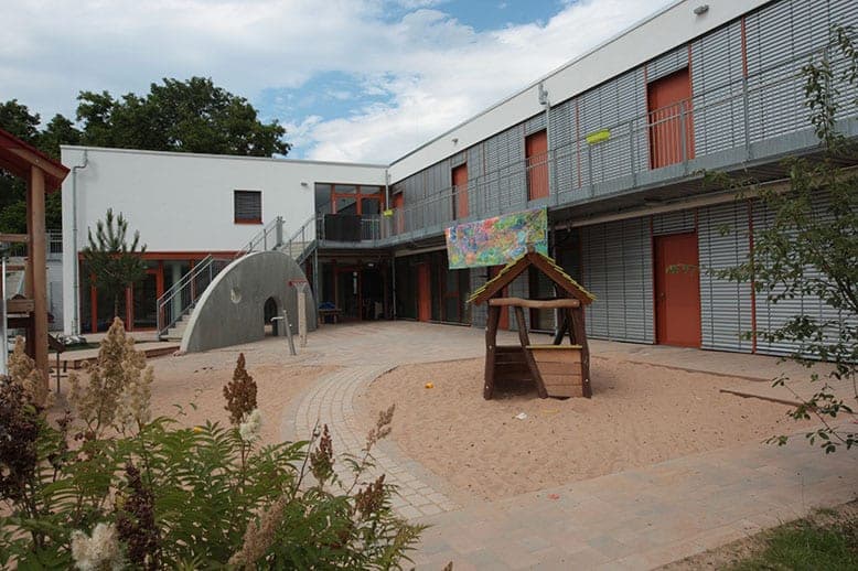 Courtyard in Zerzabelshof with a play hut in the sand, concrete arch and access gallery with sun louvres