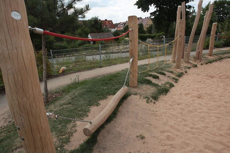 Balancing course of timber posts, ropes and a suspended log at the edge of the sand playground