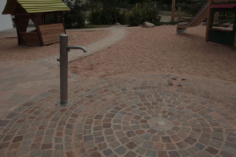 Water tap on circular natural stone paving next to the sand play area