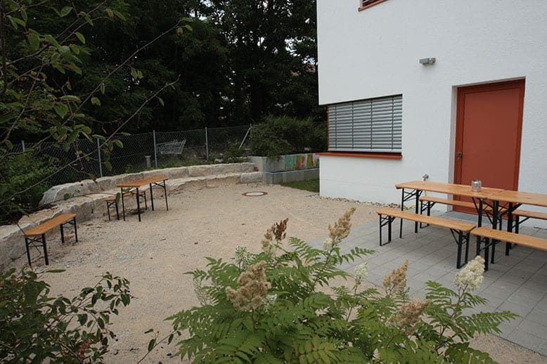 Seating area with trestle tables and benches by the building and in front of a natural stone wall