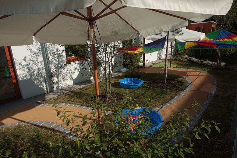 Garden with parasols, colourful canopies, paddling pools and a curving path with stone edging