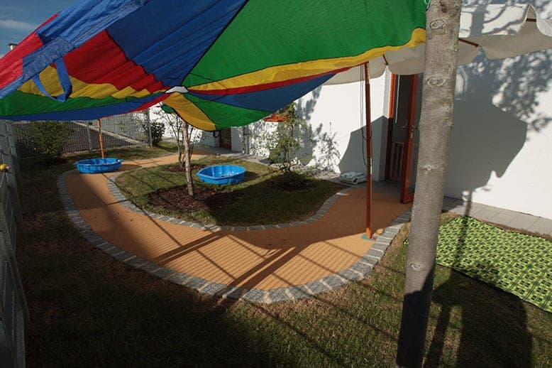 Colourful sunshade above the curving garden path with paddling pools beside the building