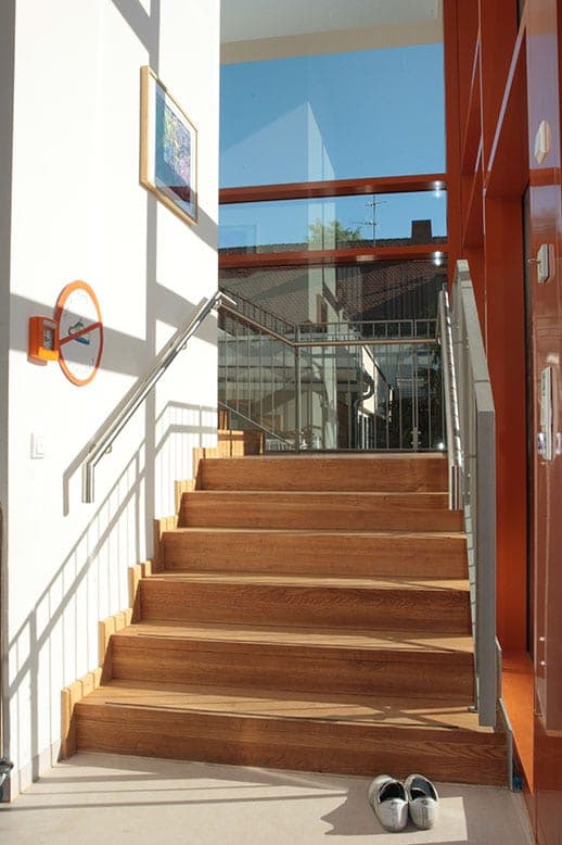 Internal staircase with timber treads and a glass balustrade in front of the tall glazed stairwell façade