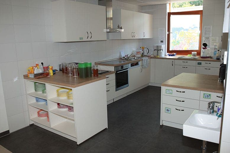 Kitchen with white fitted units, an island and colour-sorted children's crockery on open shelves