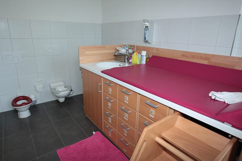Nappy-changing room with a changing table, children's steps, child-height toilets and a washbasin