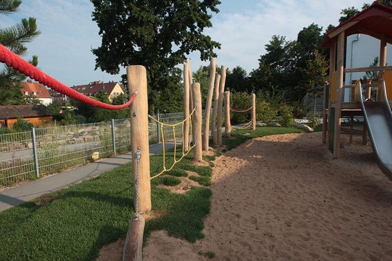 Balancing course of timber posts with red and yellow ropes along the garden fence in evening light