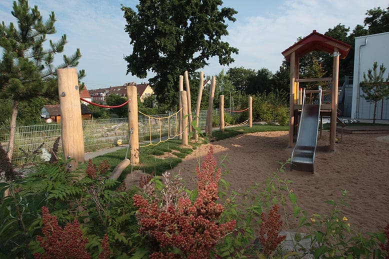 View over flowering shrubs to the play tower with slide and the balancing course