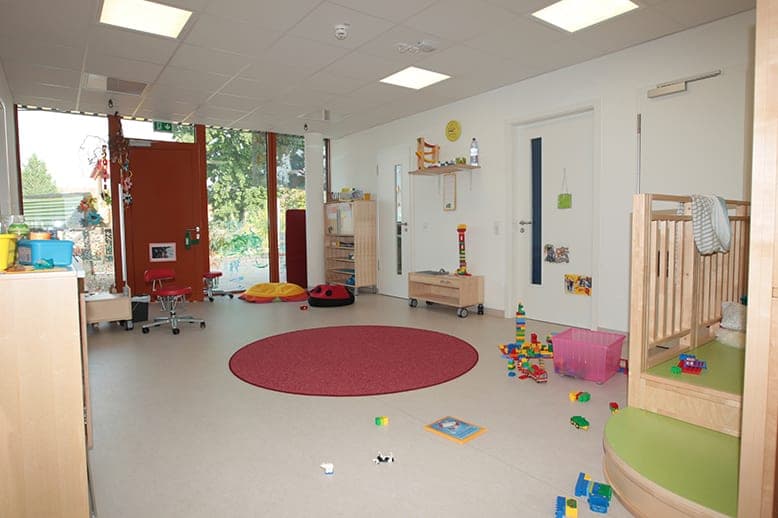 Crèche group room with a round red rug, building blocks and a play platform with wooden railings