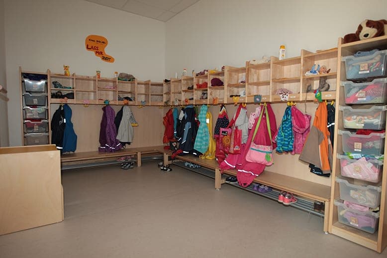 Cloakroom with timber benches, cubbies, children's jackets on hooks and boxes on shelving
