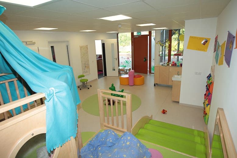 Crèche room with a play platform under a turquoise drape, green slide surface and round rug