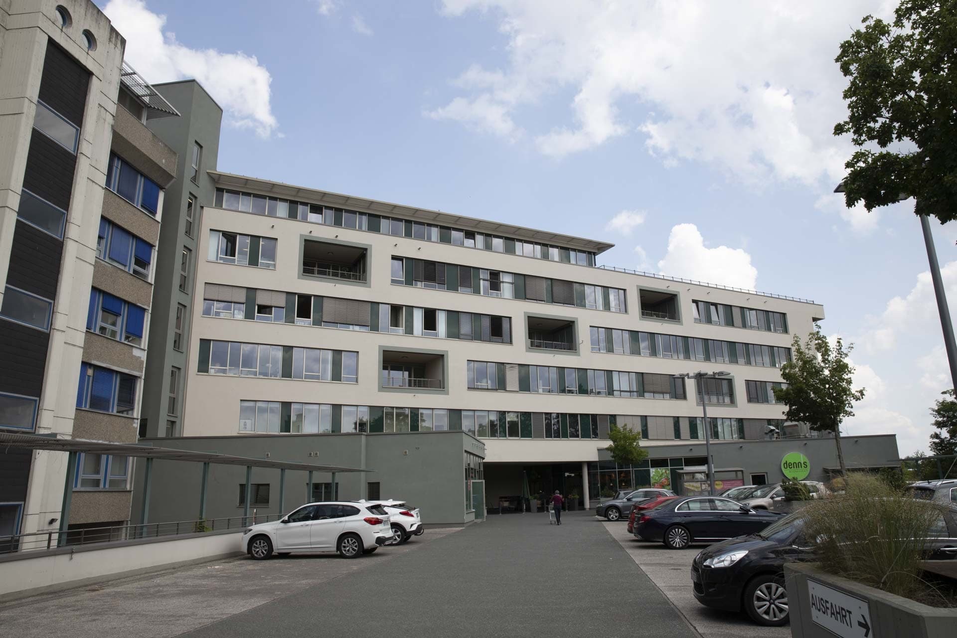 Hofseitige Fassade mit eingeschnittenen Loggien und grünen Fensterbändern über dem Parkplatz, flacher Sockelbau