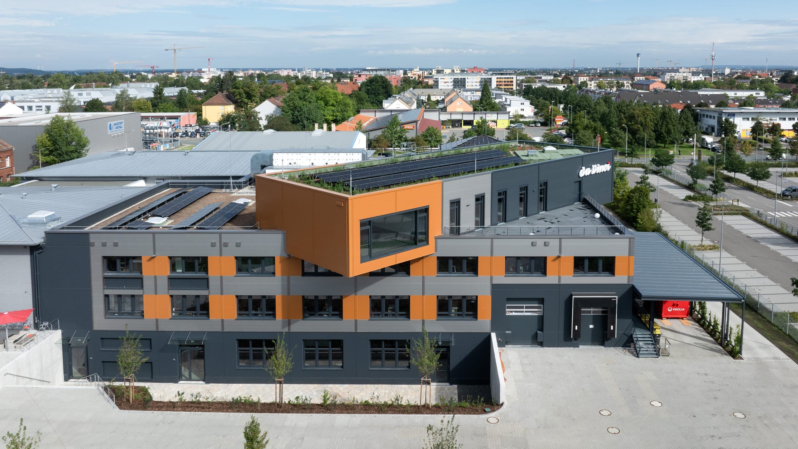 Luftbild der Hauptfassade mit auskragendem orangefarbenem Baukörper über dem Eingangsbereich