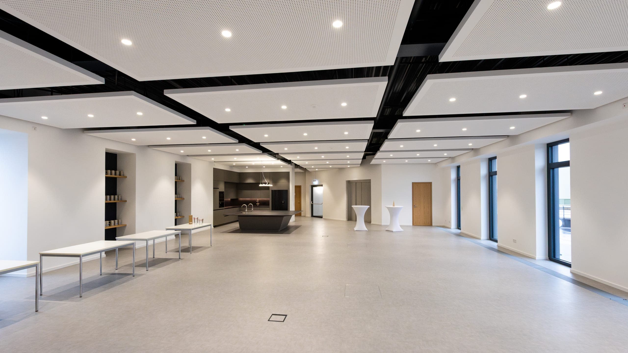 Langgestreckter Mehrzweckraum mit Kochinsel, Stehtischen und Akustiksegeln an der Decke