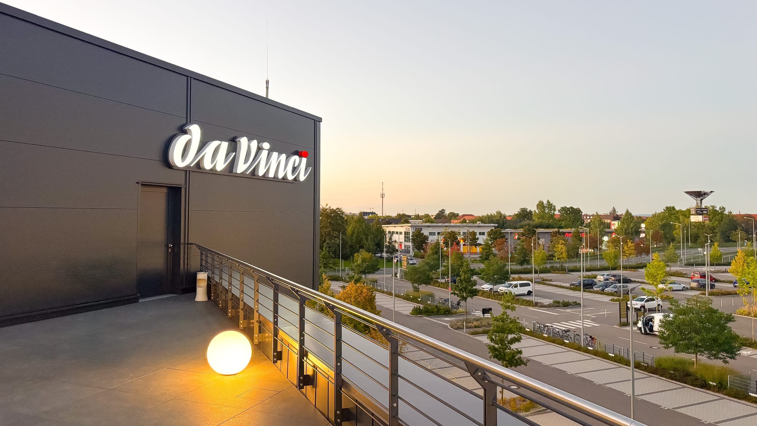 Dachterrasse in der Dämmerung mit beleuchtetem daVinci-Schriftzug und Blick über Straße und Parkplätze