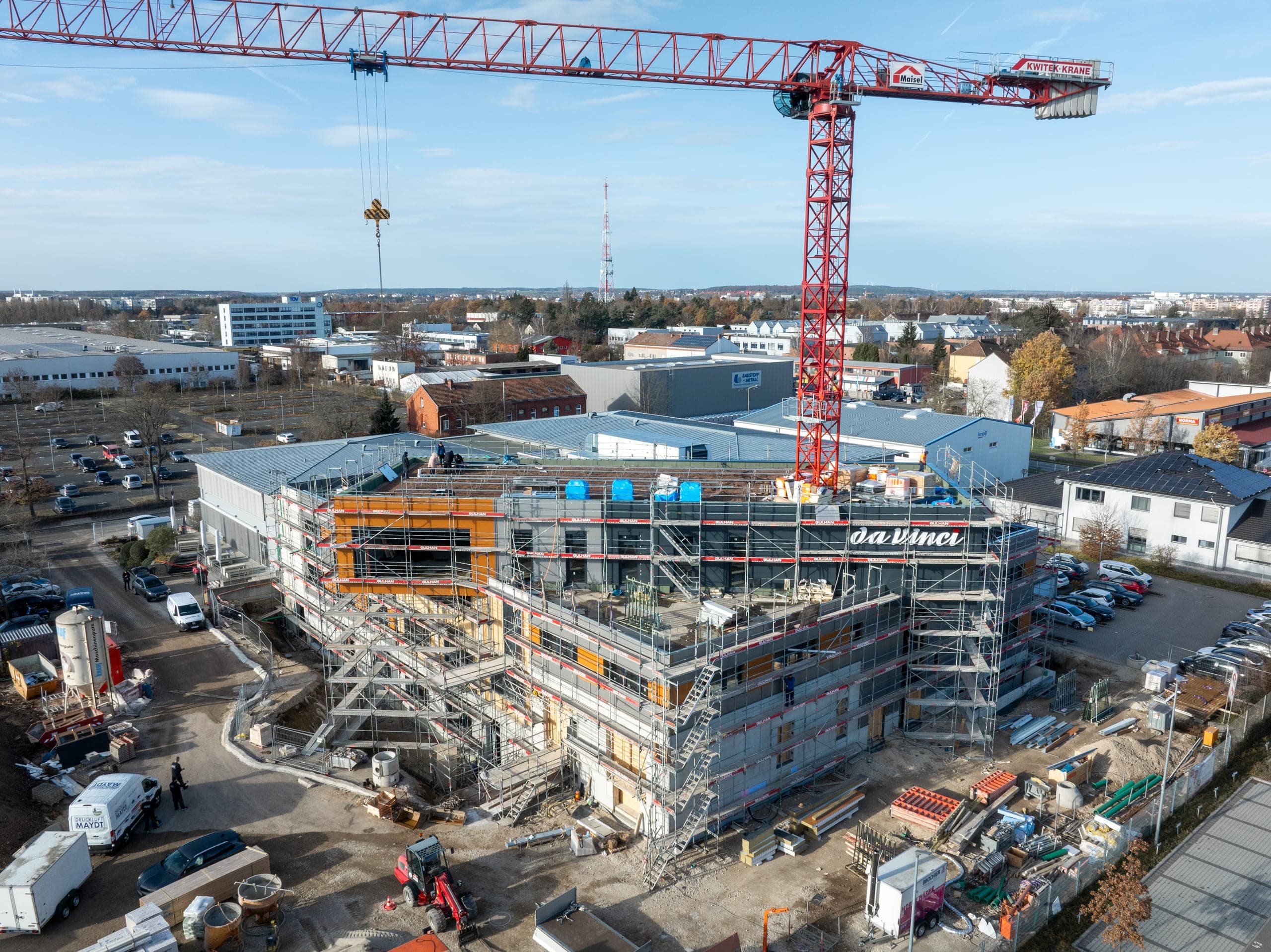 Luftbild der Baustelle mit Turmkran und vollständig eingerüstetem Neubau im Gewerbegebiet