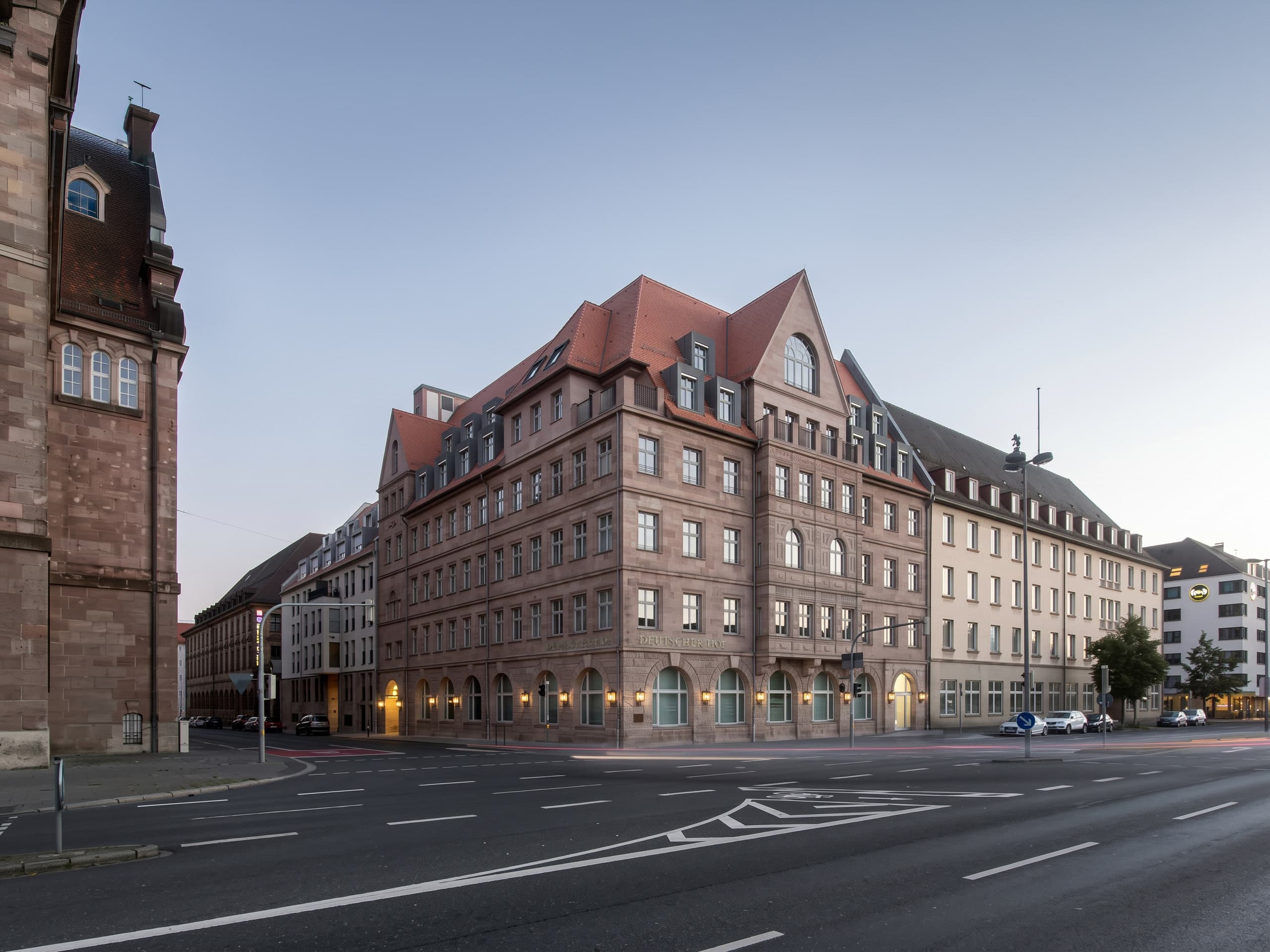 Corner view of the refurbished Deutscher Hof at dusk with lit arched windows on the ground floor