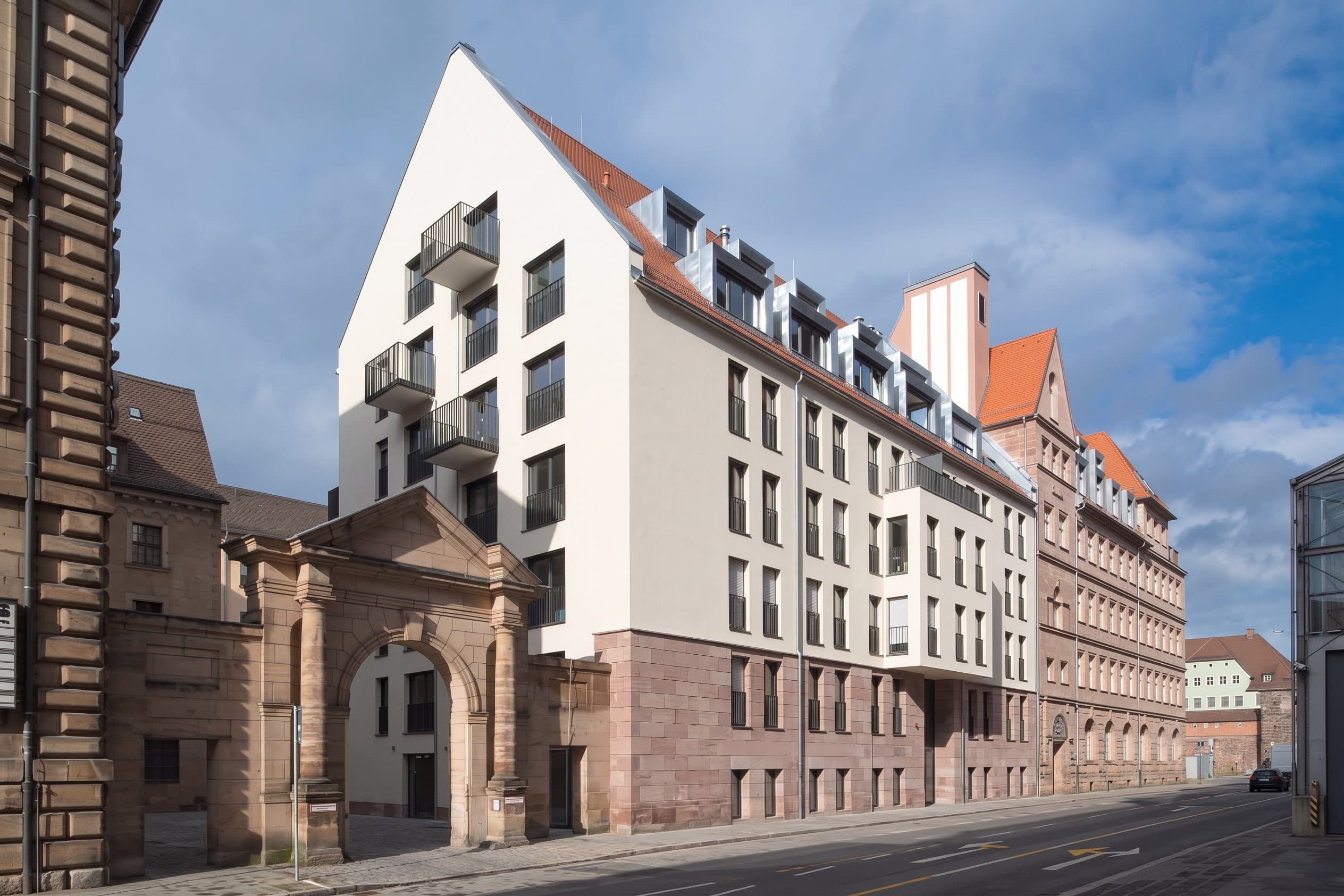 New building with balconies and a sandstone base behind the historic gateway, adjoining the old building in Nuremberg