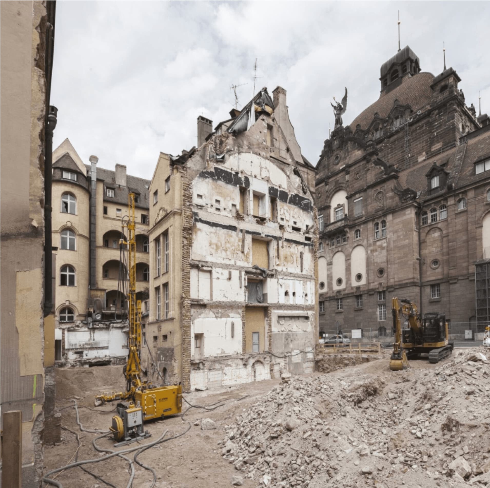 Cleared demolition site inside the block with a drilling rig and excavator, the opera house dome on the right
