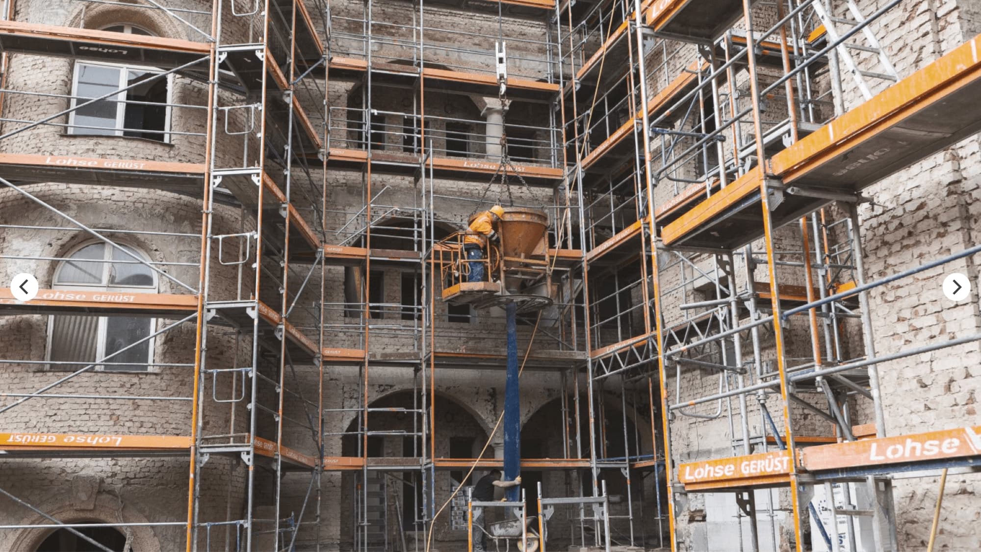 Scaffolded courtyard during the refurbishment with a concrete skip on a crane between the scaffold levels