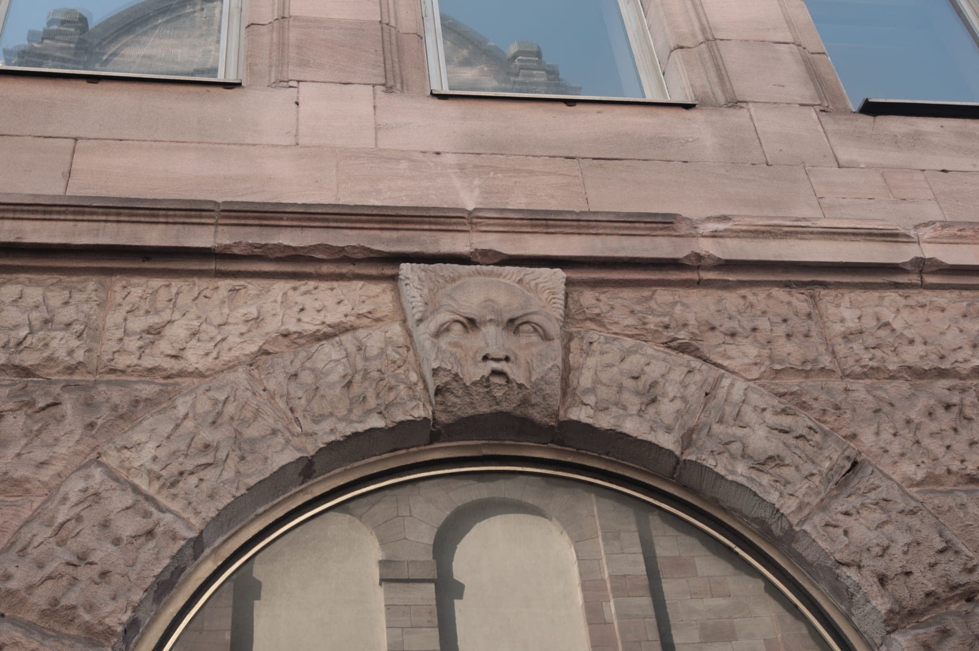 Stone mask as the keystone above an arched window in the rusticated sandstone façade