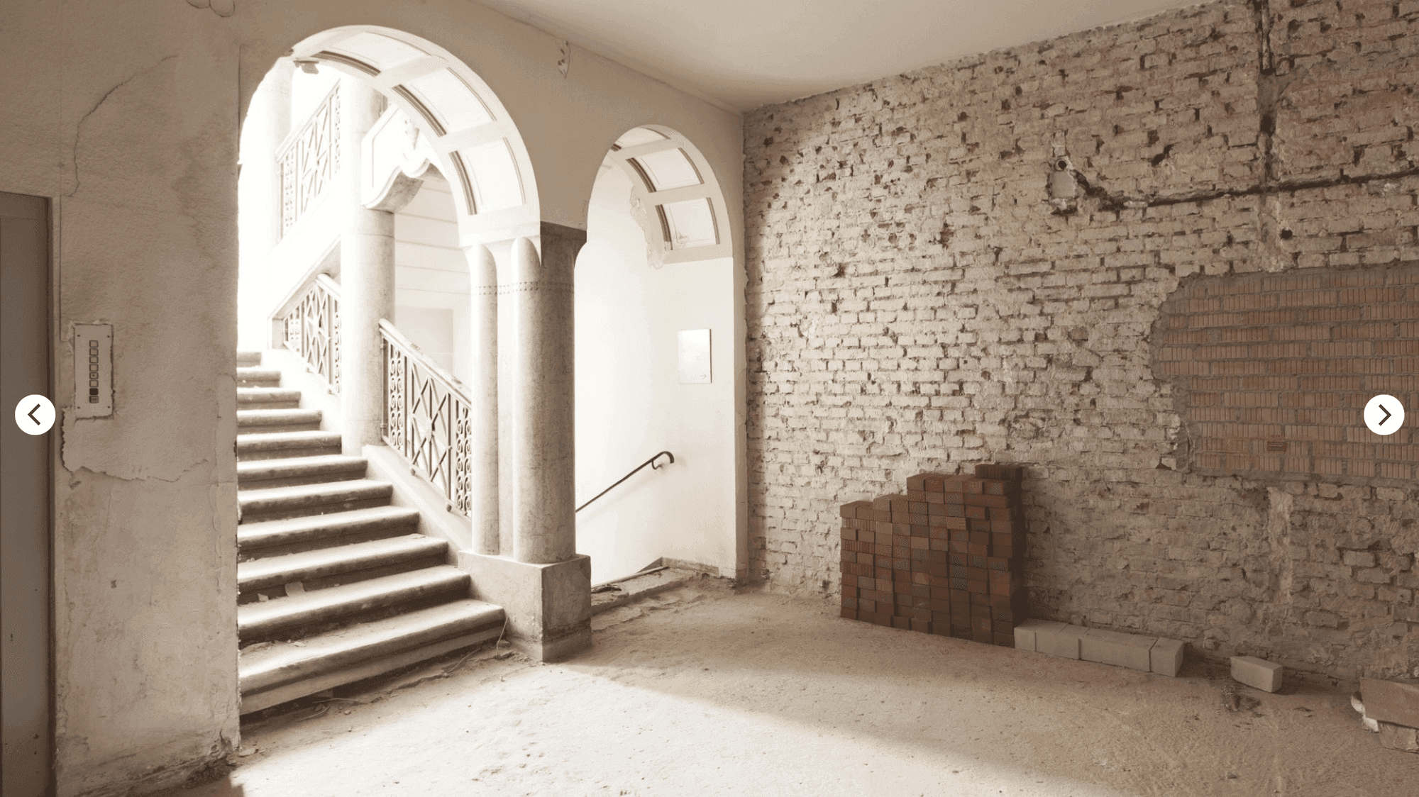Construction work in the old building with a staircase behind round arches, exposed brickwork and stacked bricks