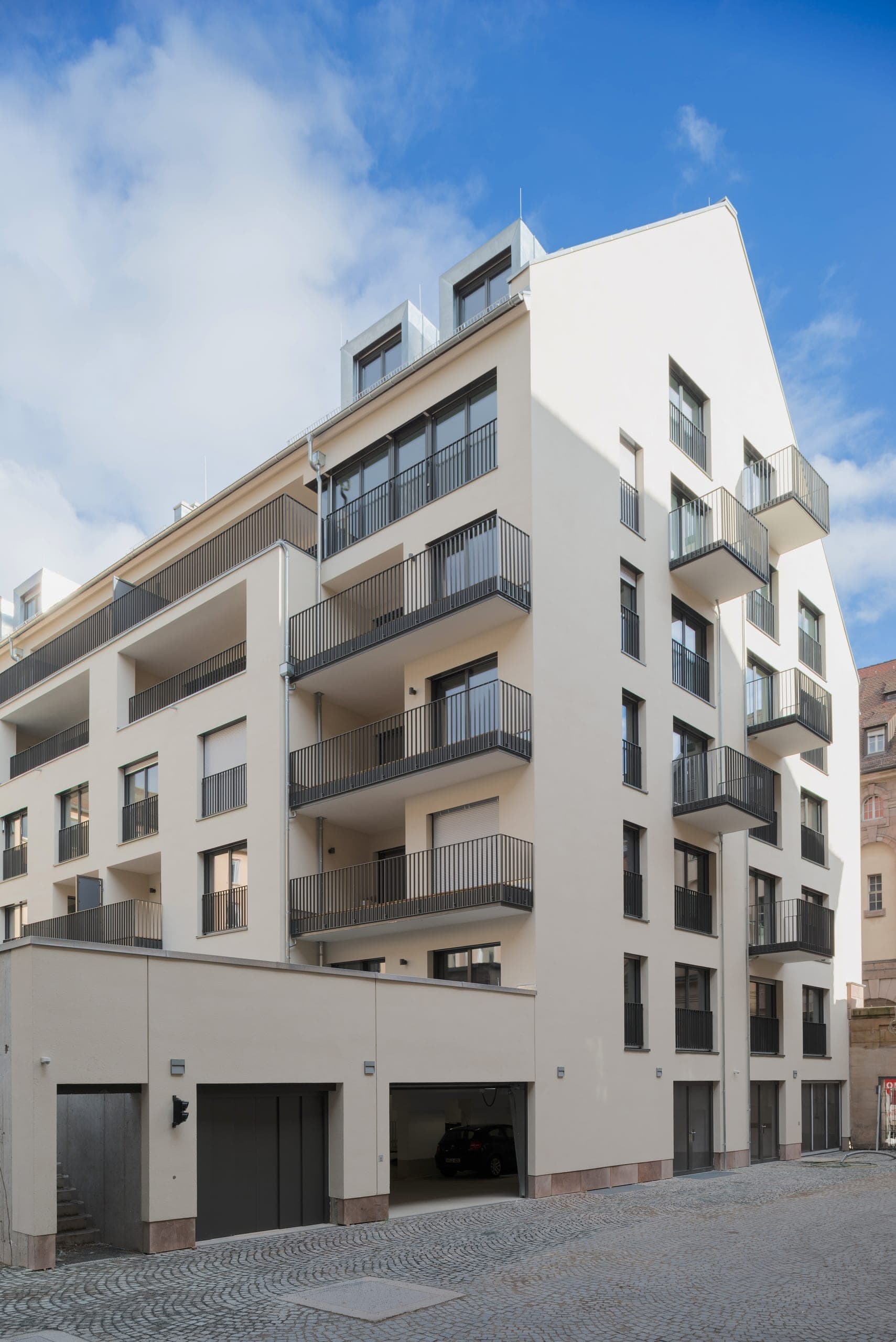 Pale new residential building with projecting balconies, dormers and garage doors on a cobbled driveway