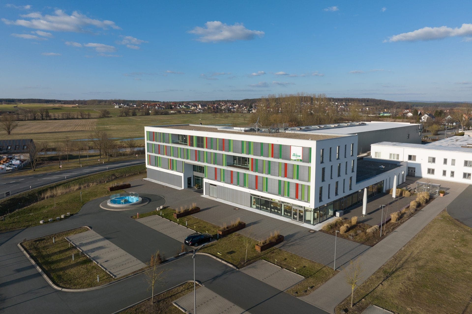 Aerial view of the administration building with coloured façade louvres and the production hall behind