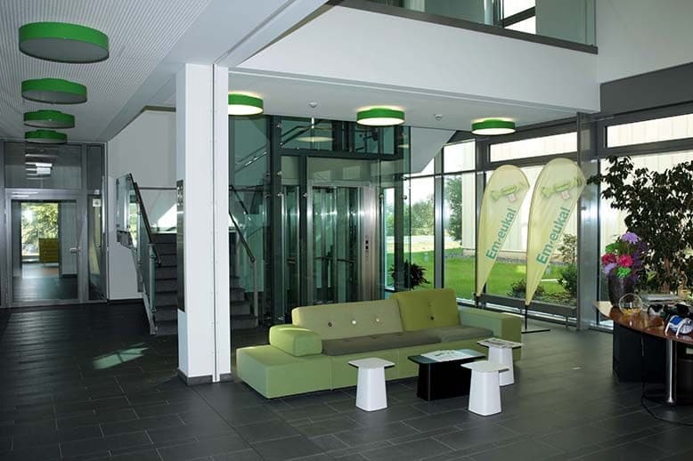 Foyer with glazed lift, staircase, green ceiling lights, seating area and promotional flags at the glass façade