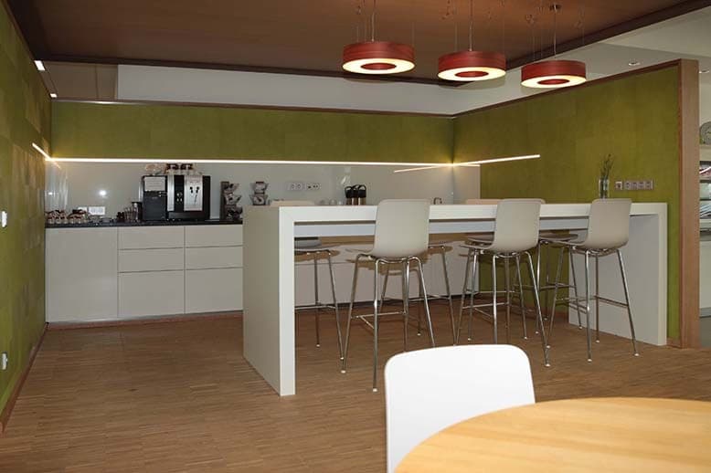 Staff kitchen with white bar counter, bar stools, red pendant lights, green-panelled walls and parquet floor