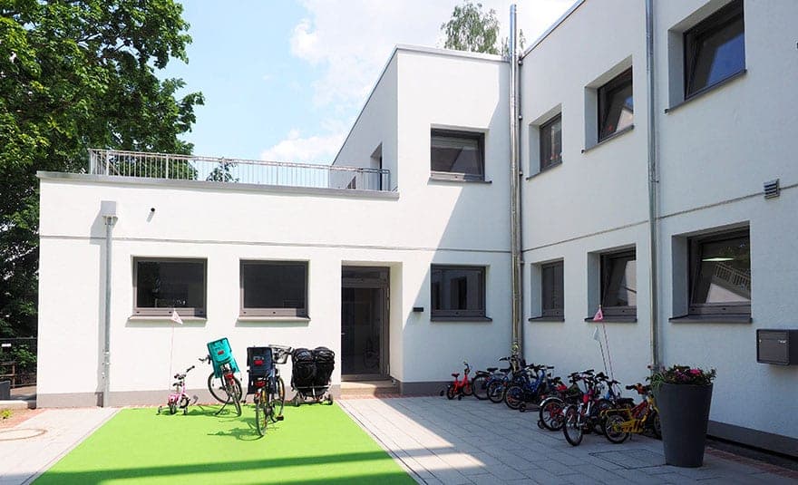 Eingangsbereich mit Kinderrädern auf Kunstrasen und Dachterrasse mit Geländer über dem Erdgeschoss