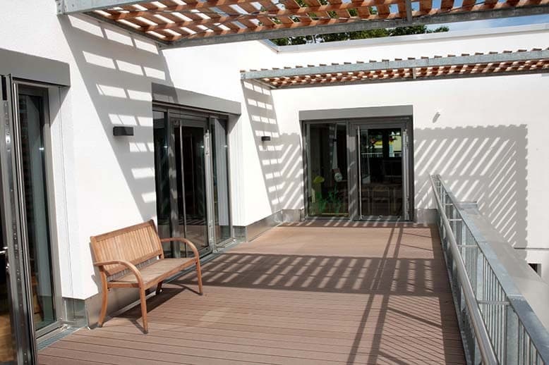 Dachterrasse mit Holzlattenpergola, Sitzbank und verglasten Türen zu den Gruppenräumen
