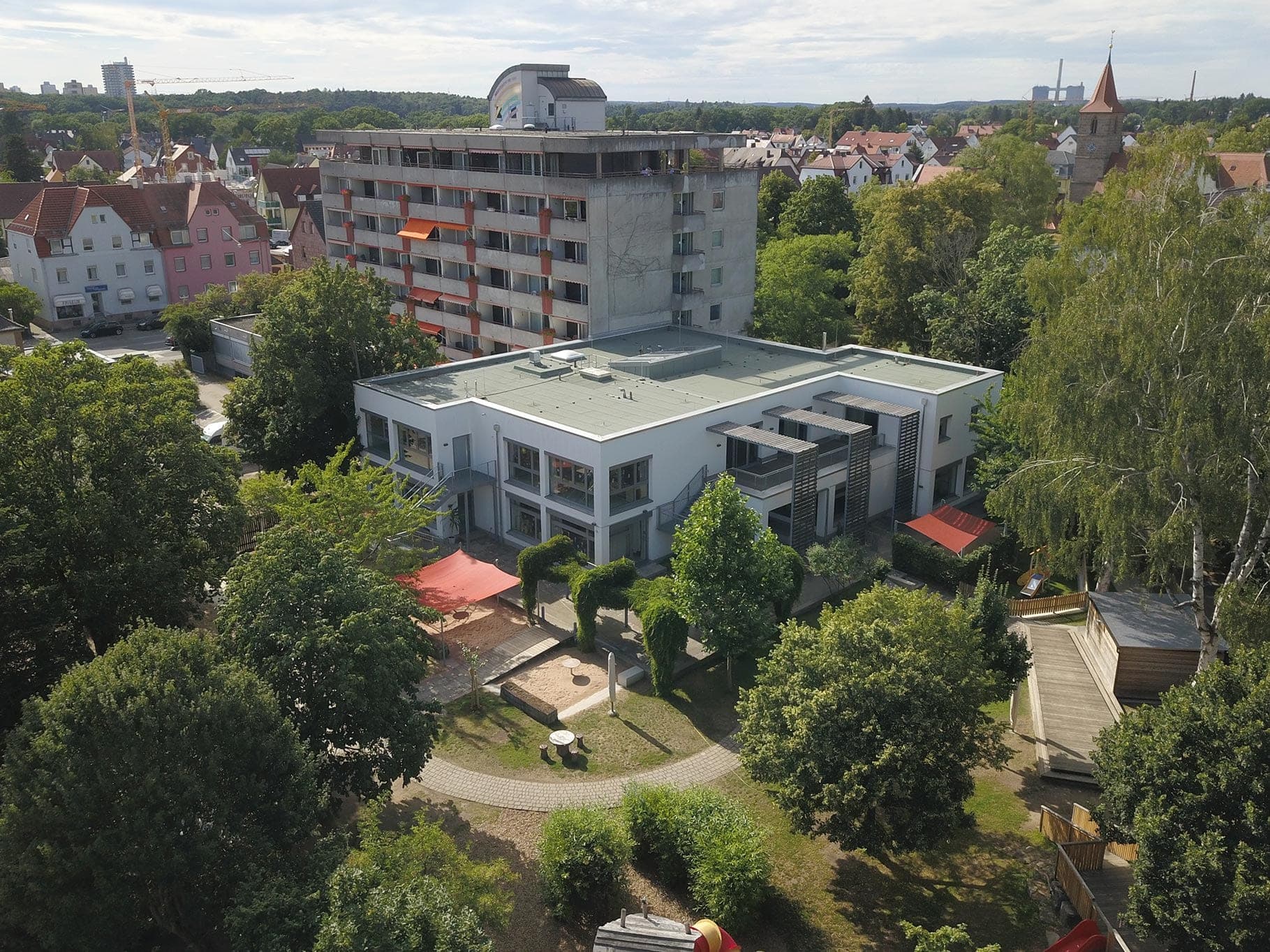 Luftbild des zweigeschossigen Kindergartens mit Garten und Spielbereich, dahinter ein Wohnhochhaus in Nürnberg