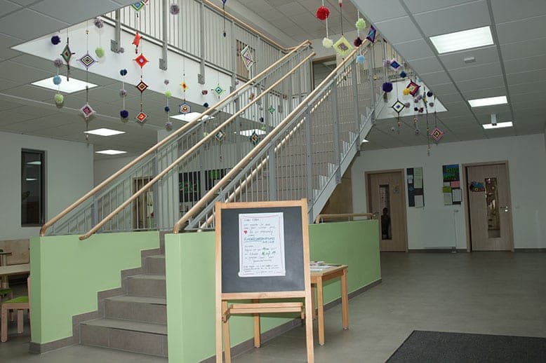 Offene Treppe mit hellgrüner Brüstung, Holzhandläufen und Infotafel auf einer Staffelei im Eingangsbereich
