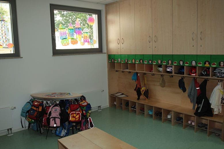 Garderobe mit Holzschränken, Haken, Schuhfächern und Kinderrucksäcken um einen runden Tisch